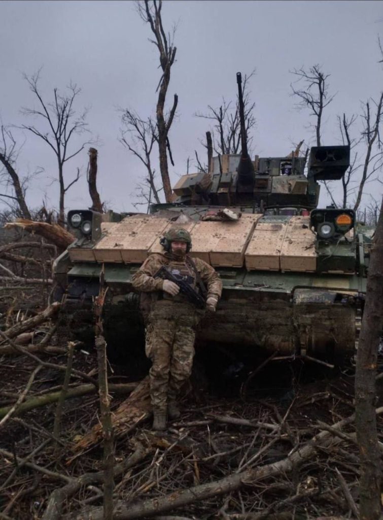Брошенная БМП M2A2 Bradley ODS-SA с ДЗ «BRAT» из 47-й мехбригады ВСУ и российский боец на ее фоне, Авдеевское направление