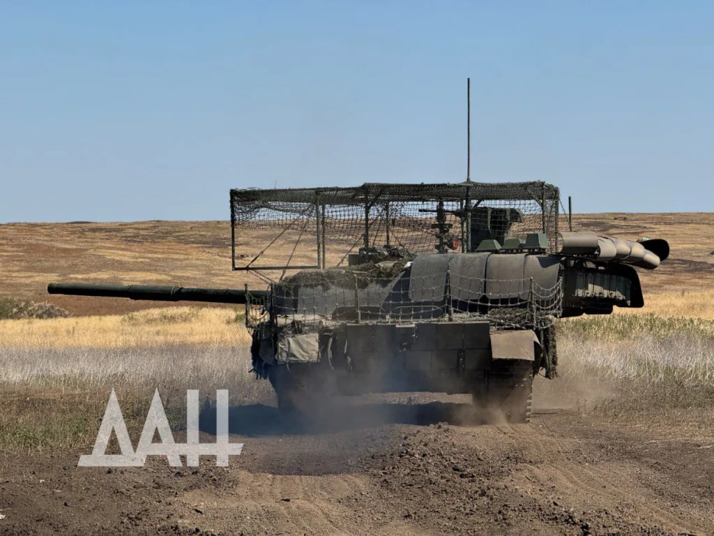 Все сложнее узнаваемый Т-90М с антидроновым козырьком, "Накидкой" и резинотканевыми лопухами на полигоне