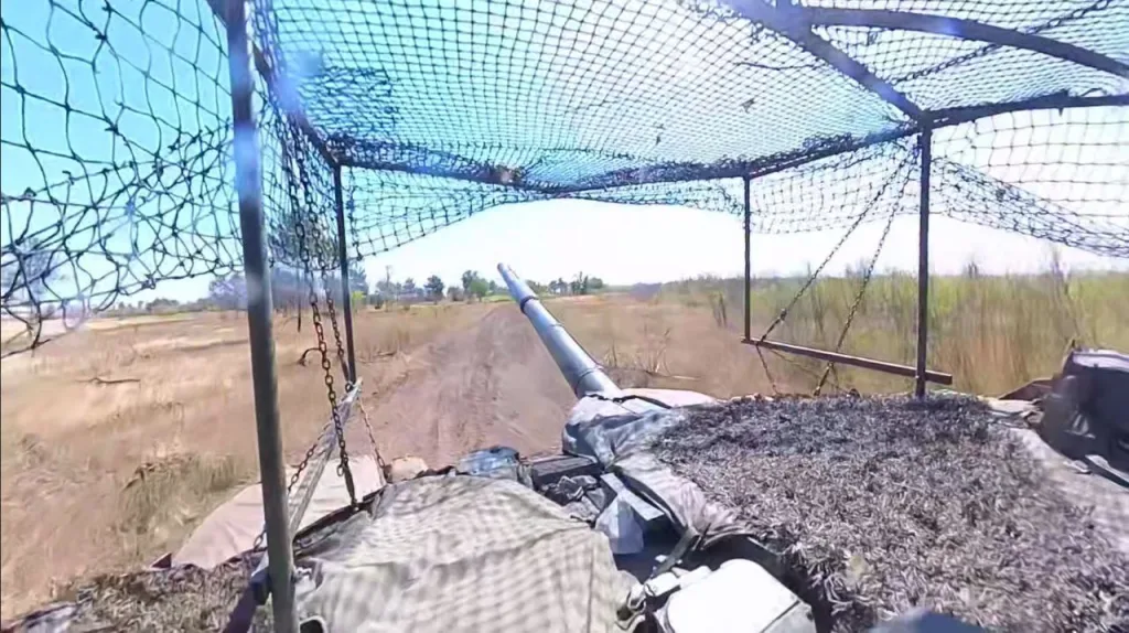 Все сложнее узнаваемый Т-90М с антидроновым козырьком, "Накидкой" и резинотканевыми лопухами на полигоне